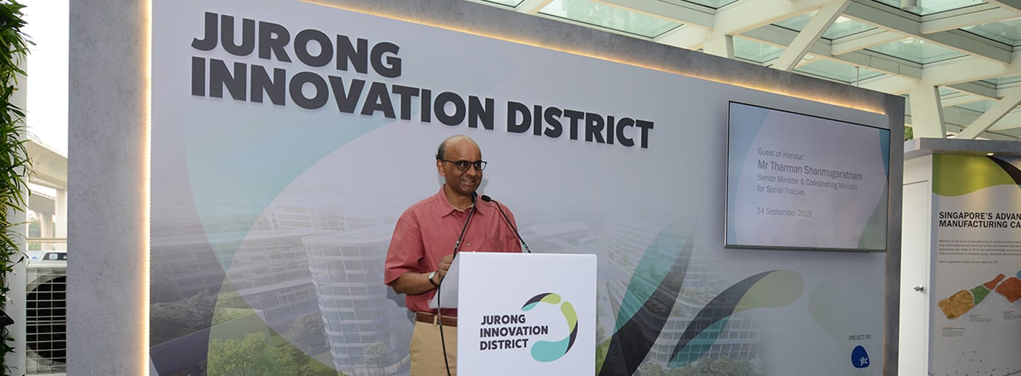 Man speaking at a podium for "Jurong Innovation District" in front of a screen.